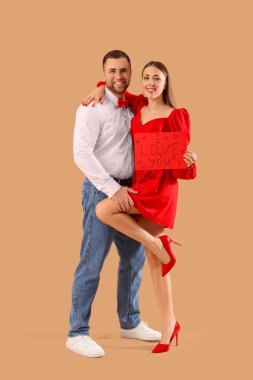 Lovely couple holding greeting card with text I LOVE YOU on beige background. Valentine's Day celebration