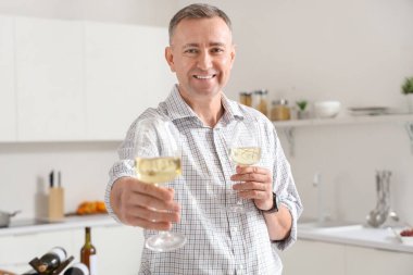 Mutfakta şarap kadehleri olan yakışıklı olgun bir adam.