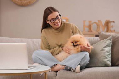 Young woman with cute Pomeranian dog and laptop sitting at home