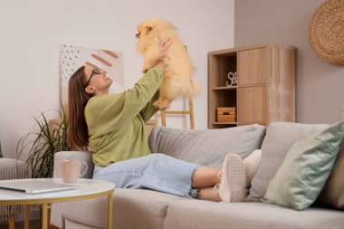 Pomeranya köpeği olan genç bir kadın evdeki kanepede dinleniyor.