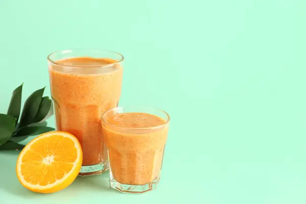 Glasses of healthy smoothie with orange and carrots on turquoise background
