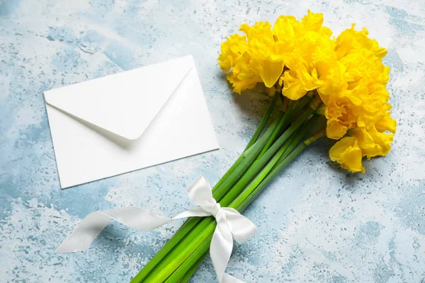 Beautiful narcissus flowers with ribbon and envelope on color grunge background