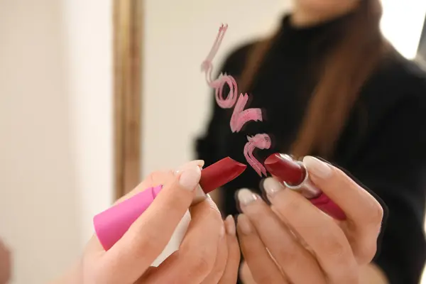 Woman writing word LOVE with lipstick on mirror