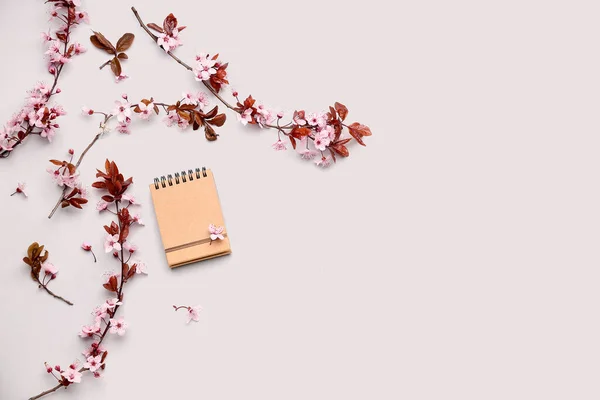 Blooming tree branches with pink flowers and notebook on white background