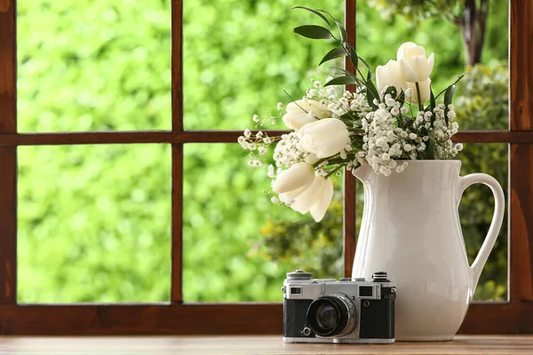 Vase with beautiful tulip flowers and photo camera on windowsill