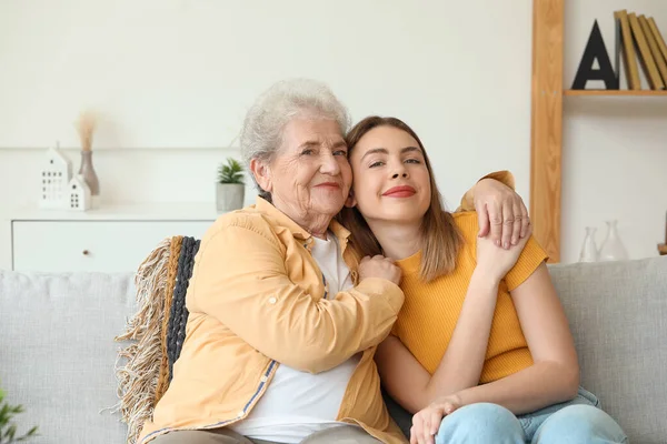 Young woman with her grandmother hugging on sofa at home