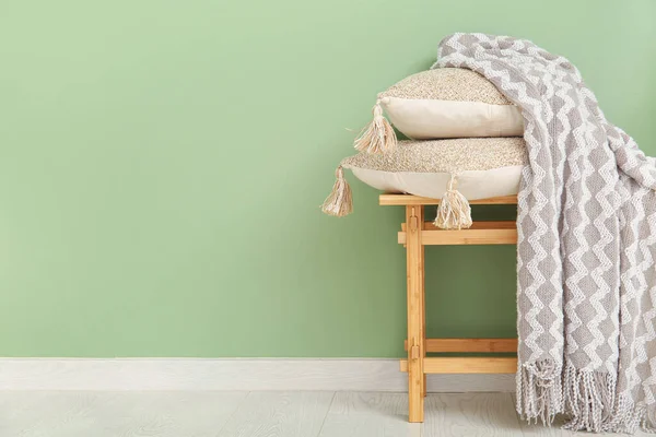Wooden bench with blanket and cushions near green wall
