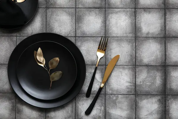 Siyah tabaklar, altın yapraklar ve gri fayanslı çatal bıçaklar.