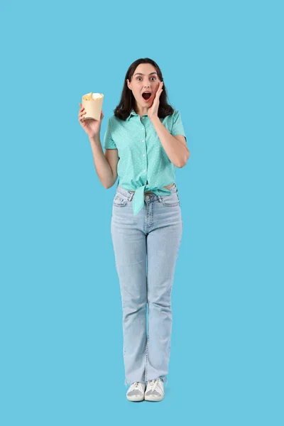 Shocked young woman with french fries on blue background
