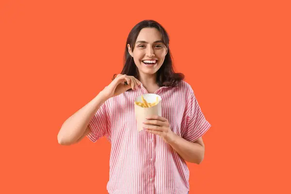 Happy young woman with french fries on orange background