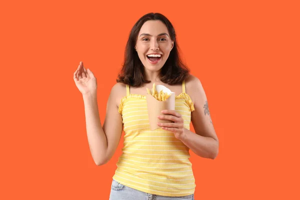 Happy young woman with french fries on orange background
