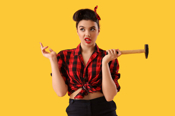 Thoughtful young pin-up woman with hammer on yellow background