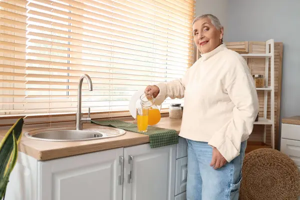 Senior woman pouring juice in kitchen