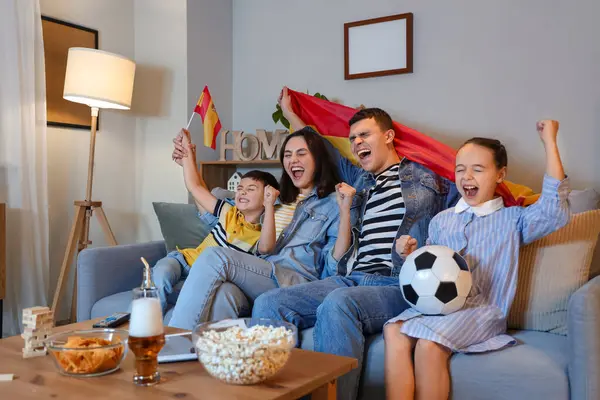 Happy family with Spanish flags watching football game on sofa at home in evening
