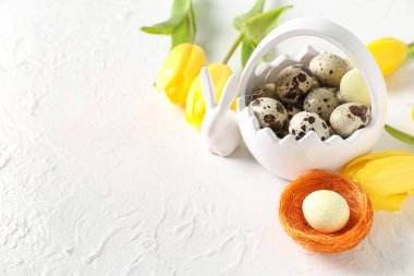 Basket with Easter quail eggs, bunny and tulip flowers on white background