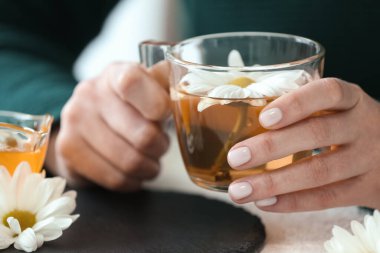 Bir fincan çay, bal ve beyaz masada güzel kasımpatılar olan kadın elleri.