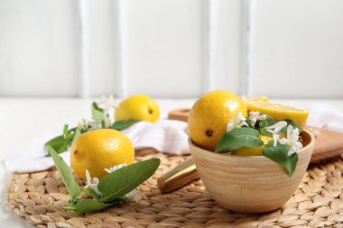 Beyaz masanın üzerinde çiçek açan dalları olan bir kase limon.