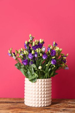 Kırmızı duvarın yakınındaki ahşap masada östoma çiçekleri olan vazo.