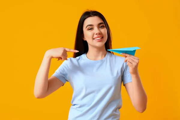 黄色の背景に紙飛行機を指している若い女性 — ストック写真