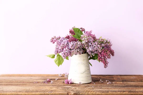 Bouquet of lilacs in vase on wooden table near wall