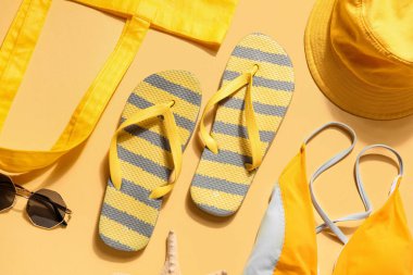 Sarı arka planda plaj aksesuarları olan parmak arası terlikler.