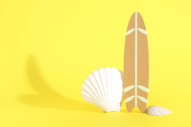 Sarı arka planda deniz kabukları olan mini sörf tahtası.