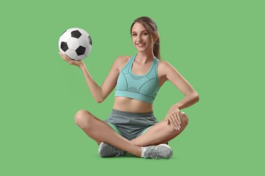 Yeşil arka planda oturan futbol toplu güzel genç bayan.