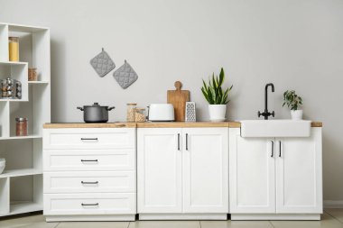 Modern mutfağın içinde mutfak aletleri, lavabo ve elektrikli soba beyaz tezgahlarda.