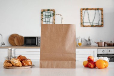 Mutfaktaki masada taze meyve ve kruvasan bulunan kağıt alışveriş torbası.