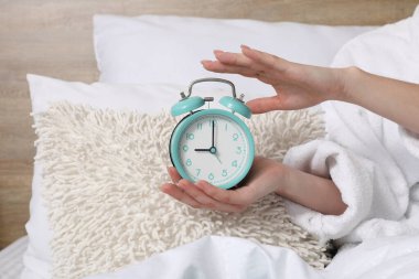 Pijamalı bir kadın, elinde çalar saatle yatakta uzanıyor, yakın plan.