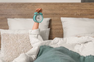 Yatakta yatarken pijamalı bir kadın çalar saati tutuyor.