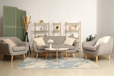 Modern oturma odasının içinde şık bir halı, gri kanepe, sehpa ve koltuklar.