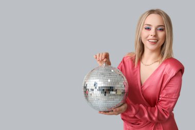 Gri arka planda disko topu olan güzel genç bir kadın.