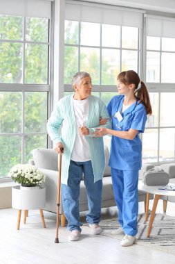 Genç bakıcı, yaşlı kadının eve yürümesine yardım ediyor.