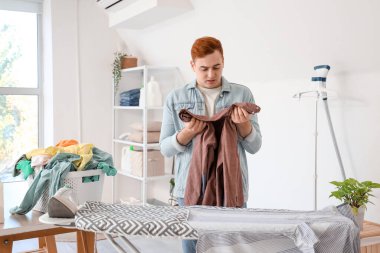 Çamaşır odasında ütü masasının yanında giysileri sıralayan genç adam.