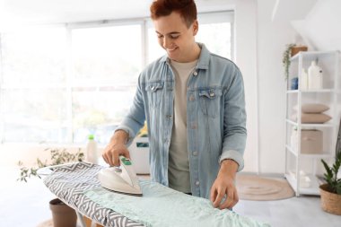 Çamaşır odasında giysileri ütüleyen yakışıklı genç adam.