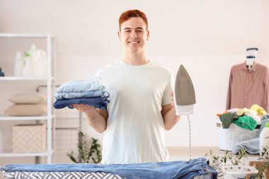 Çamaşır odasında elektrikli ütüsü ve temiz giysileri olan yakışıklı bir genç.