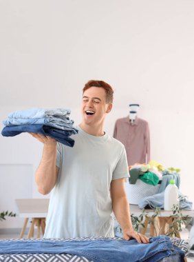 Çamaşır odasındaki ütü masasının yanında yığınla temiz elbisesi olan yakışıklı genç adam.