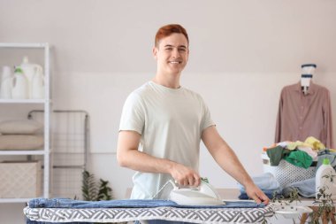 Çamaşır odasında giysileri ütüleyen yakışıklı genç adam.