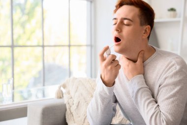 Genç adam evde boğaz spreyi kullanıyor.