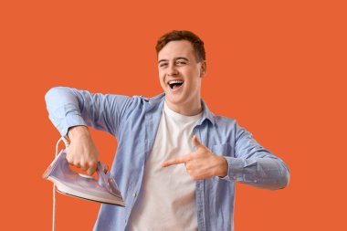 Yakışıklı genç adam turuncu arka planda modern elektrikli demire bakıyor.