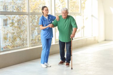 Hemşire yaşlı adama hastanede yürümesi için yardım ediyor.