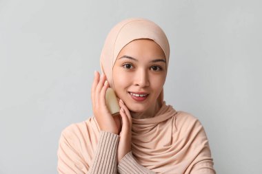 Gri arka planda bir şişe kozmetik yağıyla tesettürlü güzel Müslüman kadın.