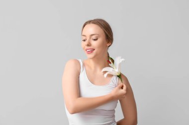 Gri arka planda zambak çiçeği olan güzel genç bir kadın.