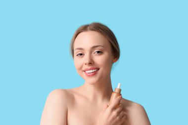 Mavi arka planda kozmetik yağı şişesi olan güzel genç bir kadın.