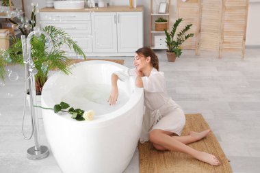 Evde küvetin yanında sabun köpüğü olan güzel bir kadın.