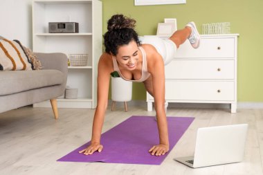 Genç Afro-Amerikalı kadın oturma odasında dizüstü bilgisayarla antrenman yapıyor.