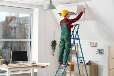 Erkek elektrikçi odada merdiven üzerinde çalışıyor.