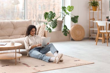 Young African-American woman using laptop on floor at home