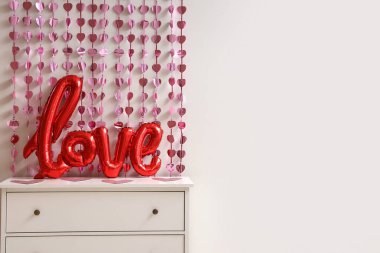 Balonlardan yapılmış aşk sözcüğü ve beyaz duvarın yanında pembe kalpler olan çekmeceler. Sevgililer Günü kutlaması